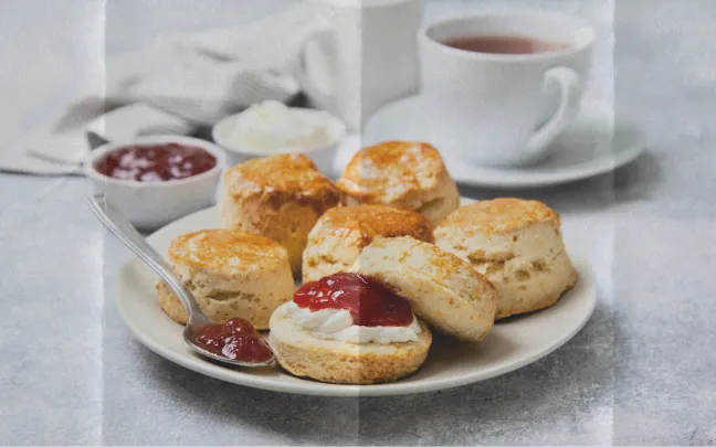 A plate of scones, served with clotted cream, jam and a cup of tea.